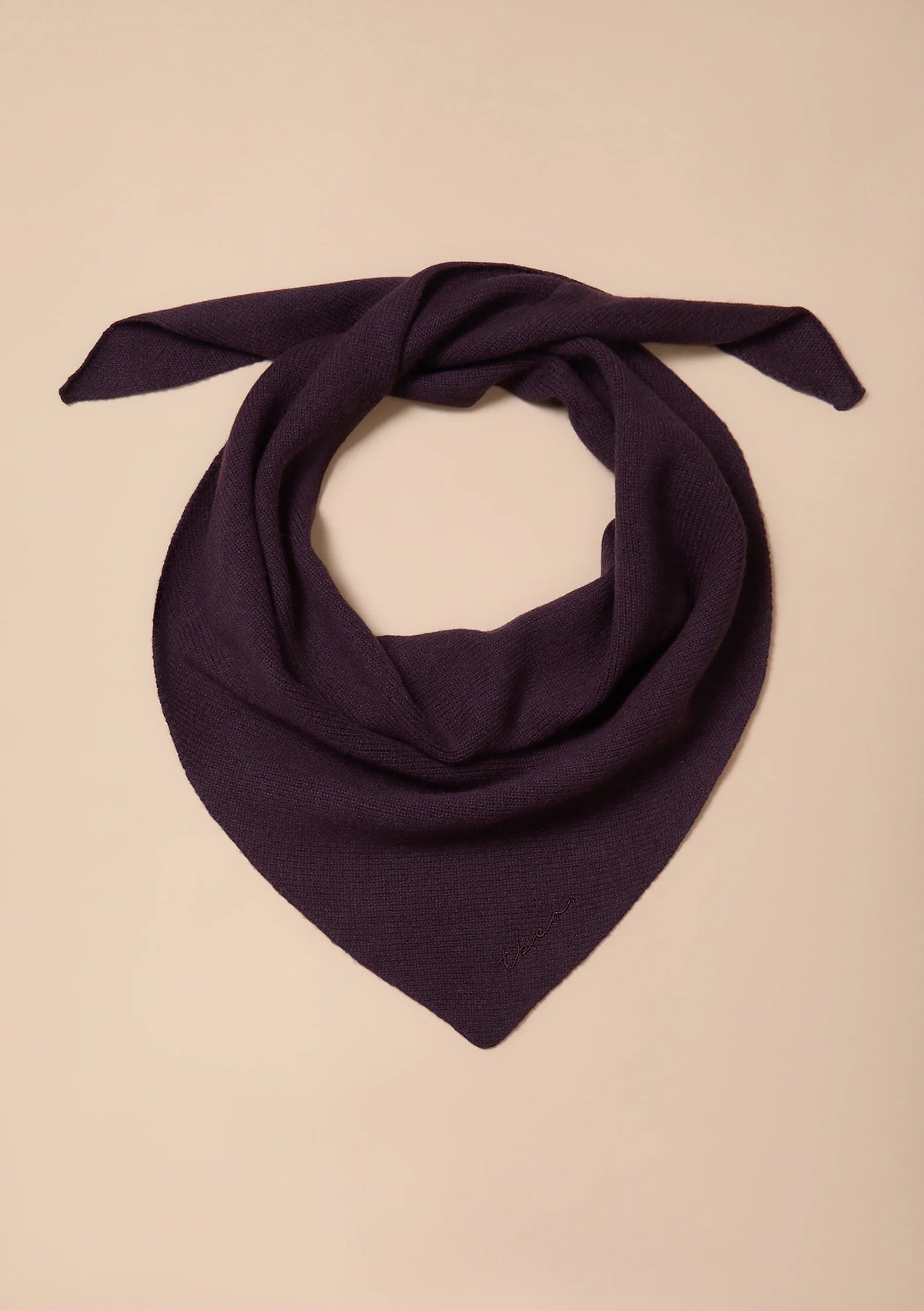 A dark purple knit bandana or neck gaiter scarf tied in a loop, displayed flat against a solid beige background.