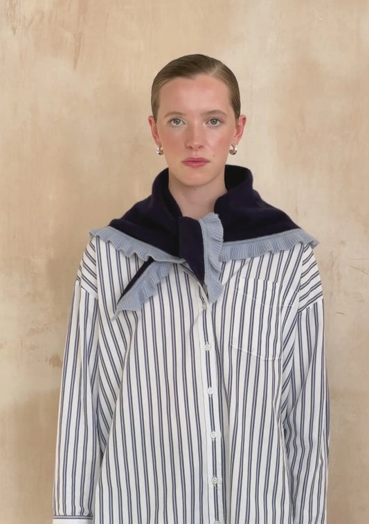 Person wearing a striped shirt with a navy and gray collar against a beige background