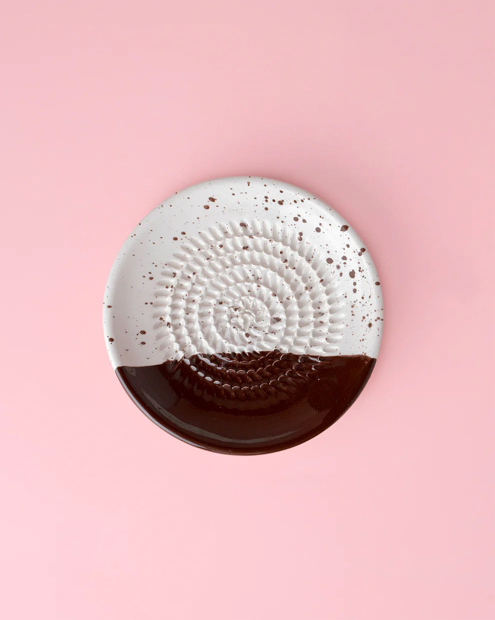 Round ceramic dish with textured white top and brown bottom on a pink background
