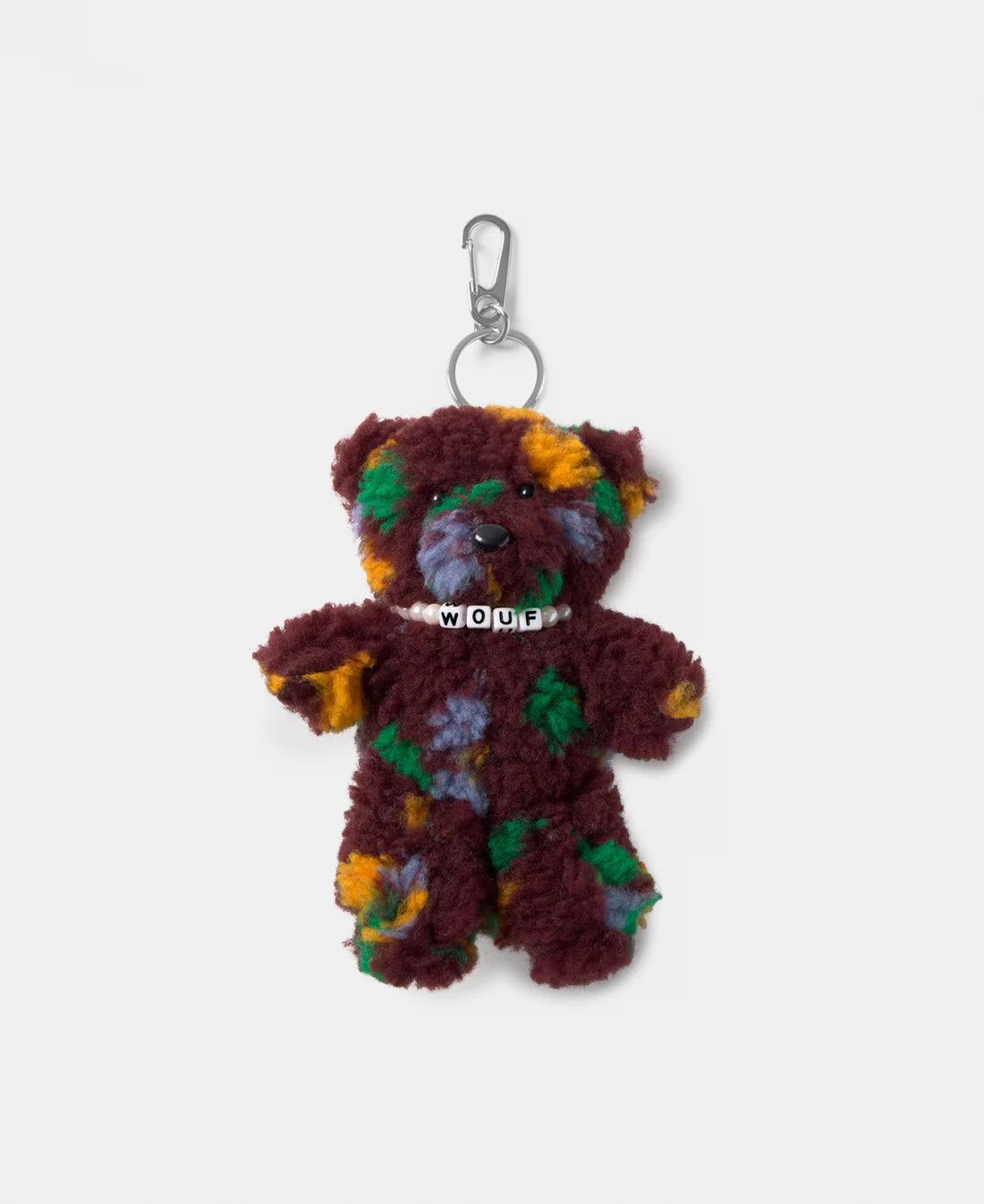 A plush teddy bear keychain or bag charm with a maroon body and multicolored patches in green, yellow, orange, and purple, featuring a silver metal clasp and a white collar with the word 'WOUF' in black letters.
