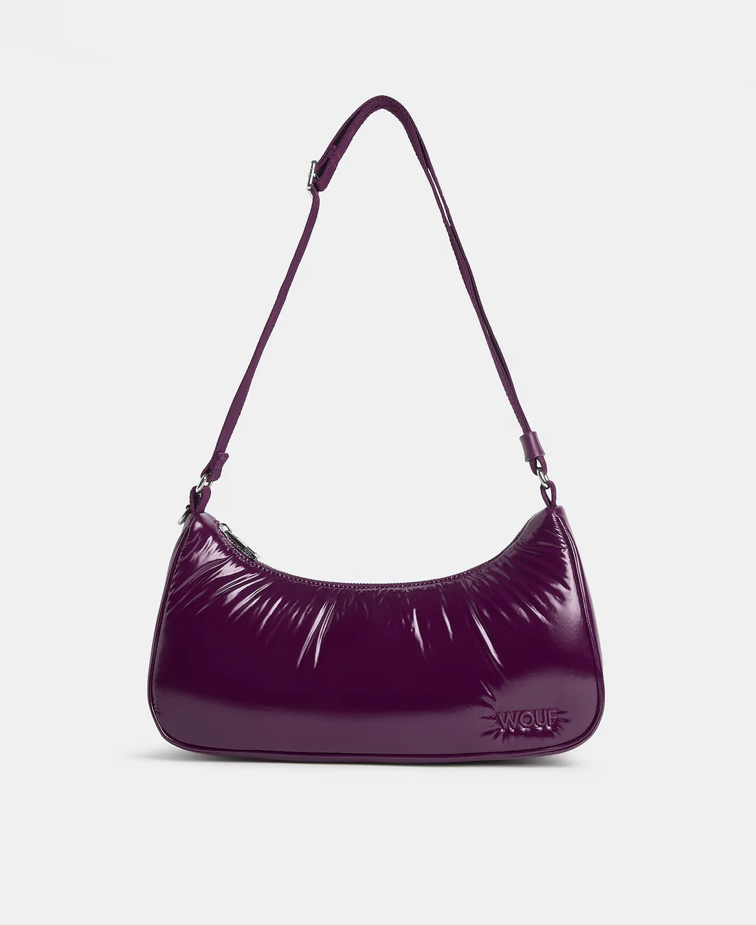 A glossy, deep purple crescent-shaped shoulder bag with a thin matching shoulder strap and a small embossed logo on the front, set against a plain light gray background.