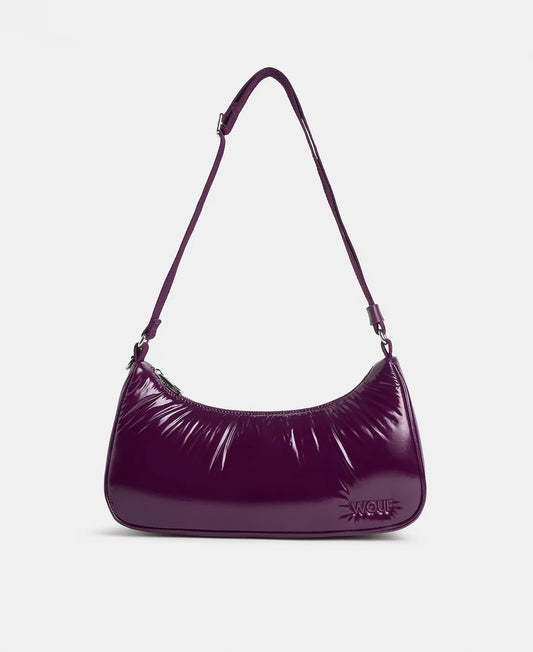 A glossy, deep purple crescent-shaped shoulder bag with a thin matching shoulder strap and a small embossed logo on the front, set against a plain light gray background.