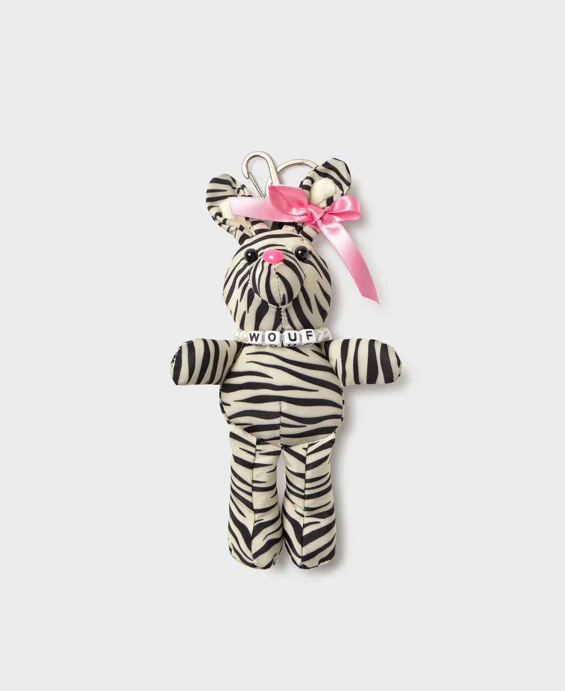 A zebra-print plush keychain shaped like a bear, featuring black and white stripes, a pink satin bow on its head, and a silver metal keyring at the top. The plush has a small white collar with the word 'MOUR' embroidered on it, set against a solid light gray background.