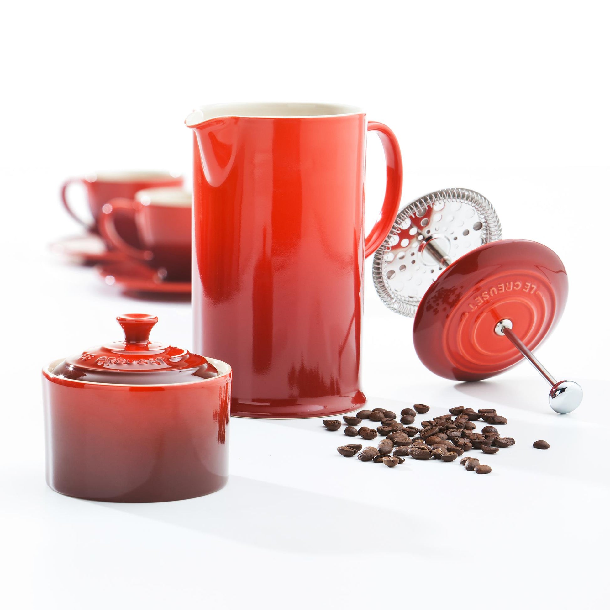 The cafetiere shown with some coffee beans, a ramekin and two cups and saucers