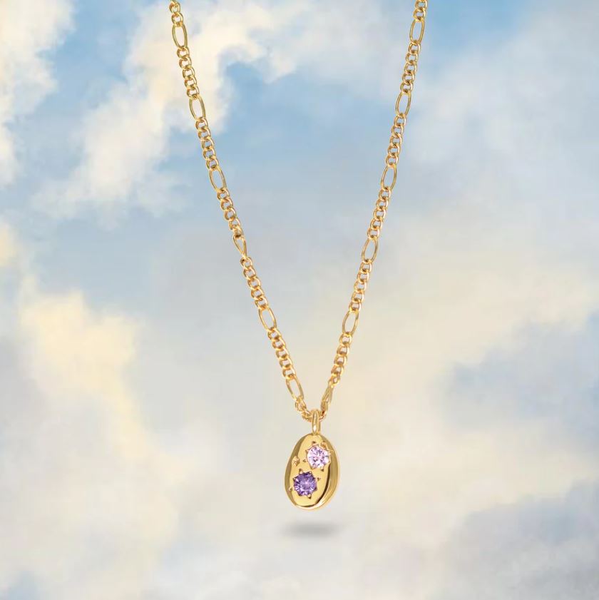 gemstone studded pebble pendant necklace in gold shown on a cloudy sky background