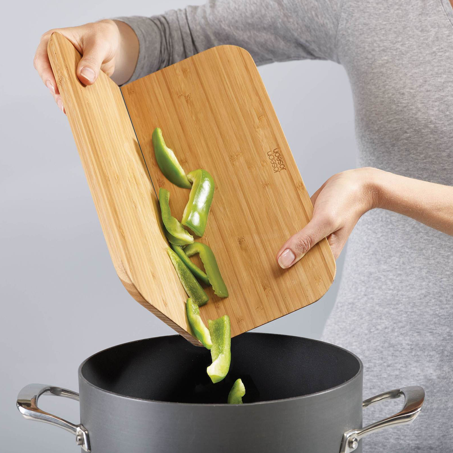 a woman pouring green peppers from the chopping board into a pot