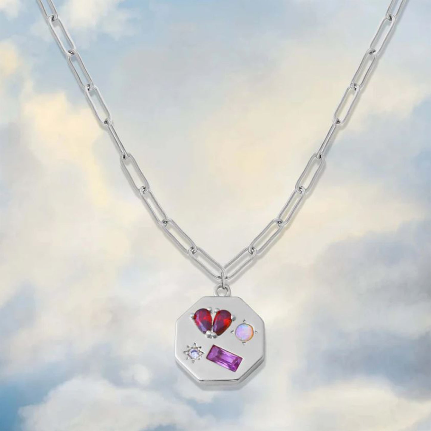 geometric silver pendant with gemstones on a cloudy sky background