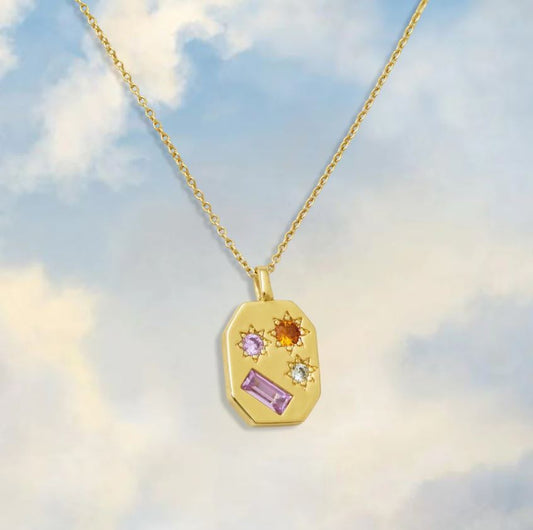 gold geometric pendant necklace with gemstones on blue sky background