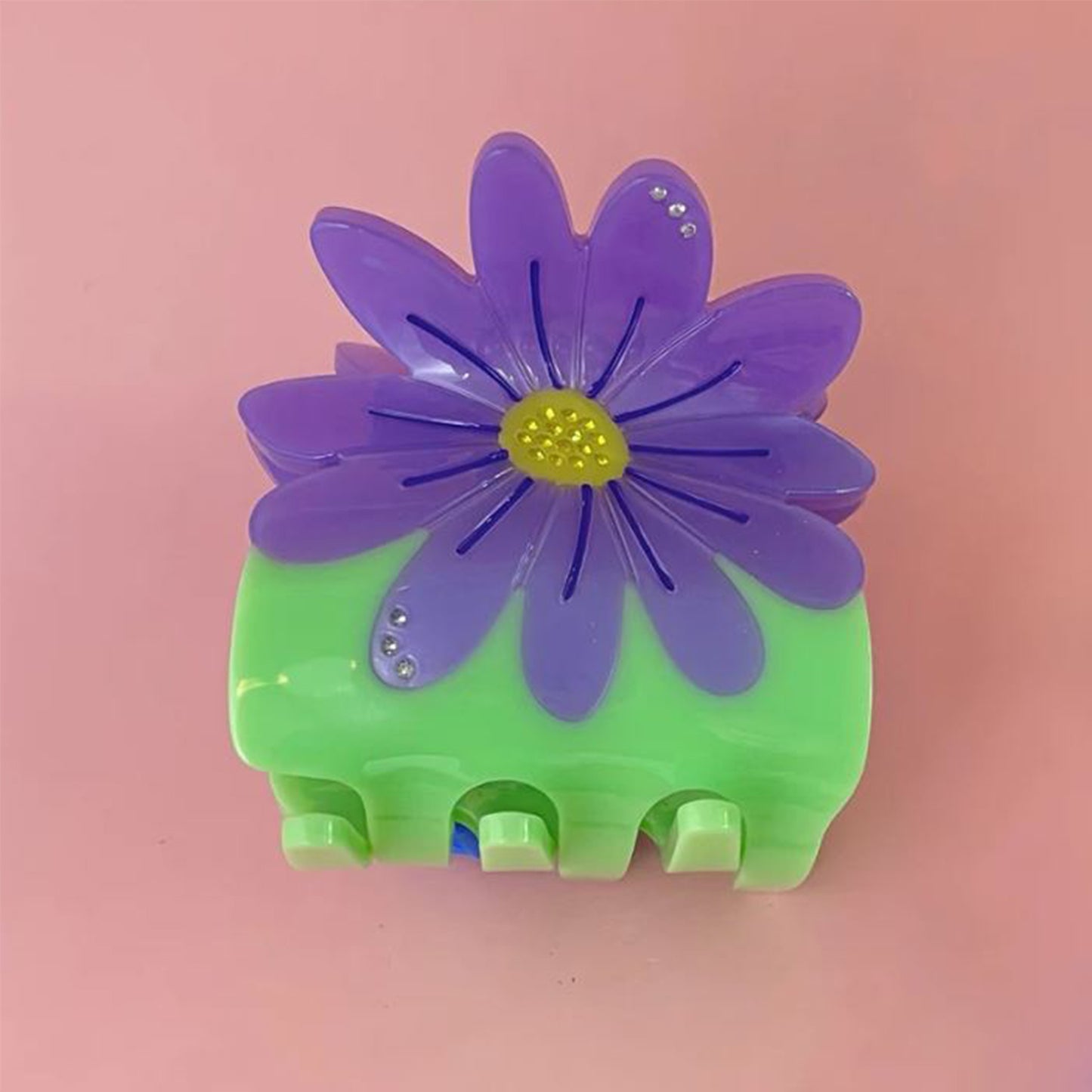 green claw clip with large purple daisy on a pink background 