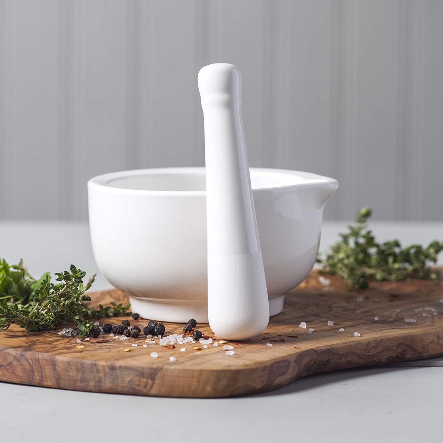 the morar and pestle on a seving board with fresh herbs and seasonings
