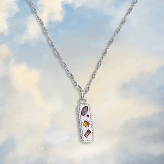 silver tag shaped necklace with colourful gemstones on a cloudy sky print background 